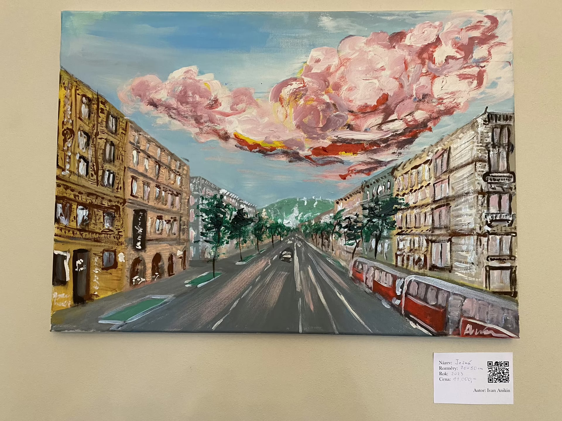 A broad city avenue recedes between historic buildings under dramatically painted pink clouds, photographed during an exhibition.
