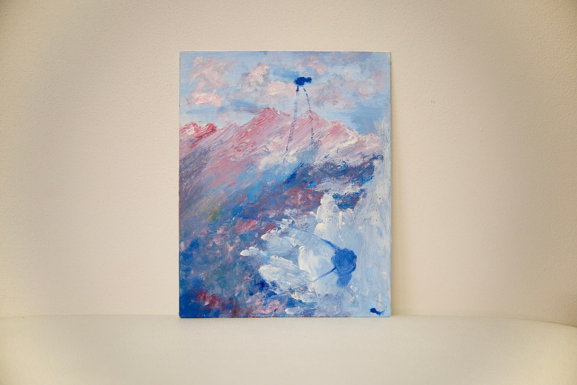 The unframed canvas standing against a plain cream wall, its blue and pink mountain scene seen straight on.