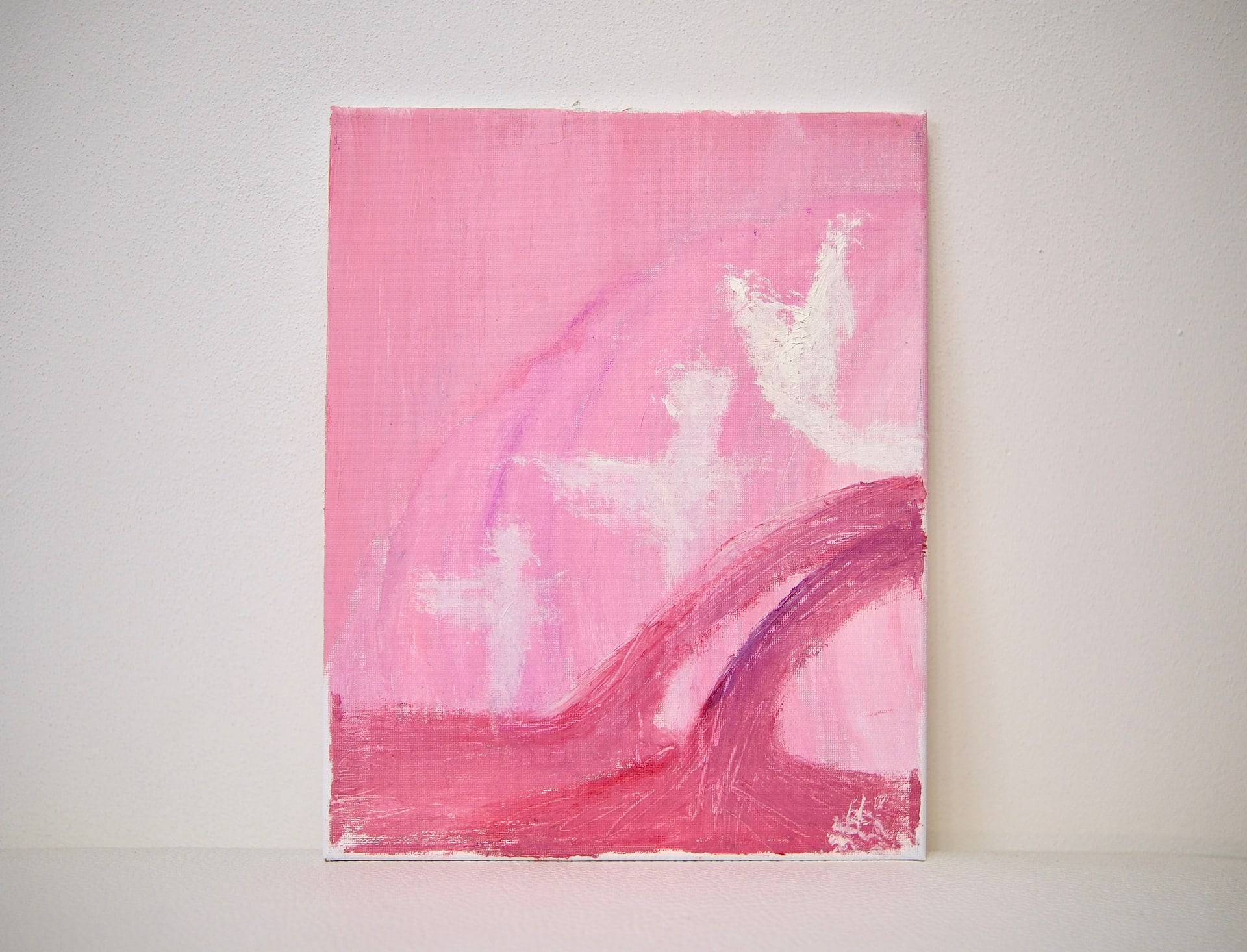 The unframed canvas propped against a white wall, its pink field and rising white figures seen straight on.