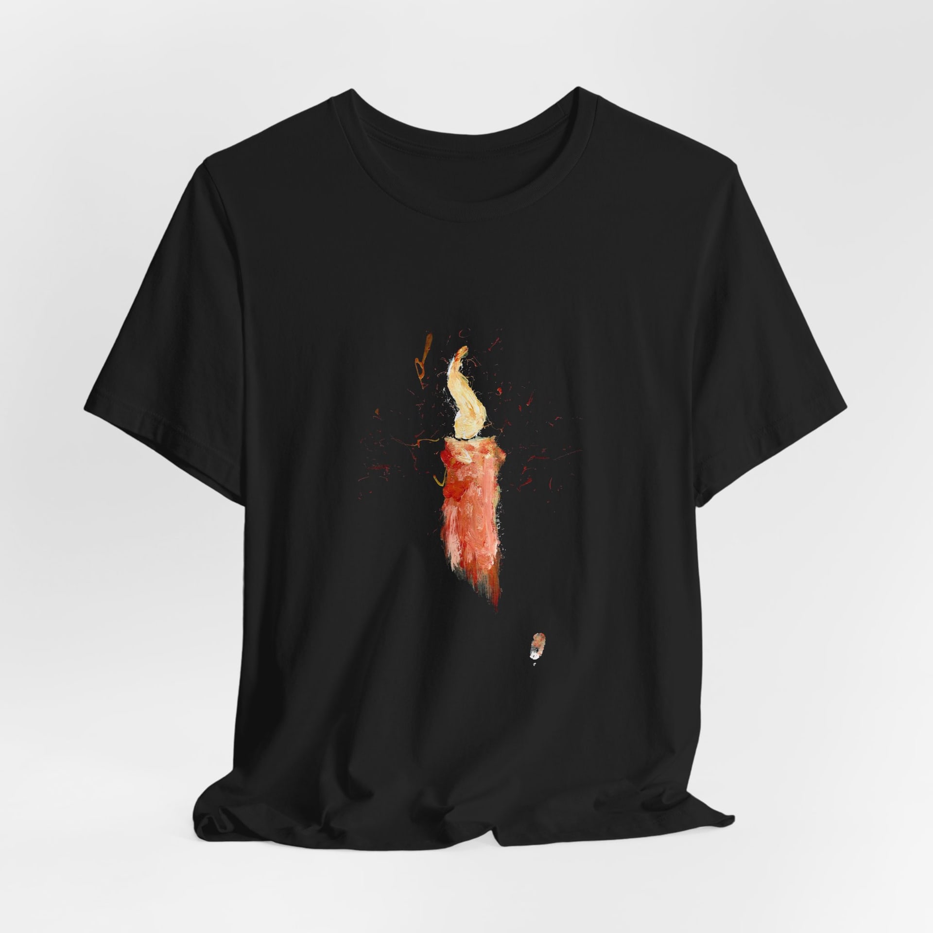 The black t-shirt hanging loose and softly draped against a pale grey background, the painted candle centred on the chest.