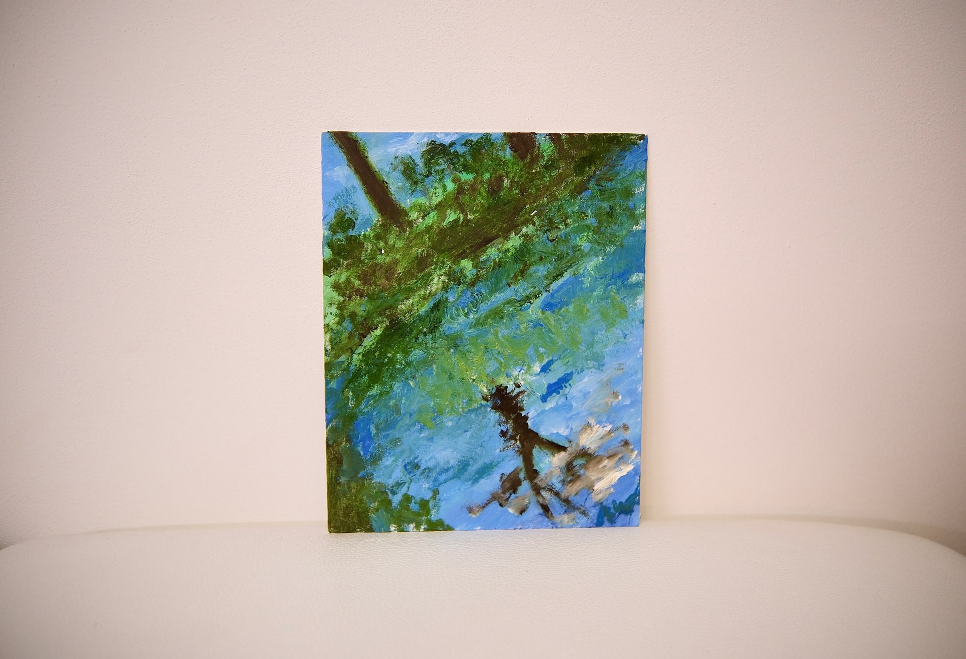 The unframed canvas propped against a warm off-white wall, its green branch and rippled blue water seen straight on.