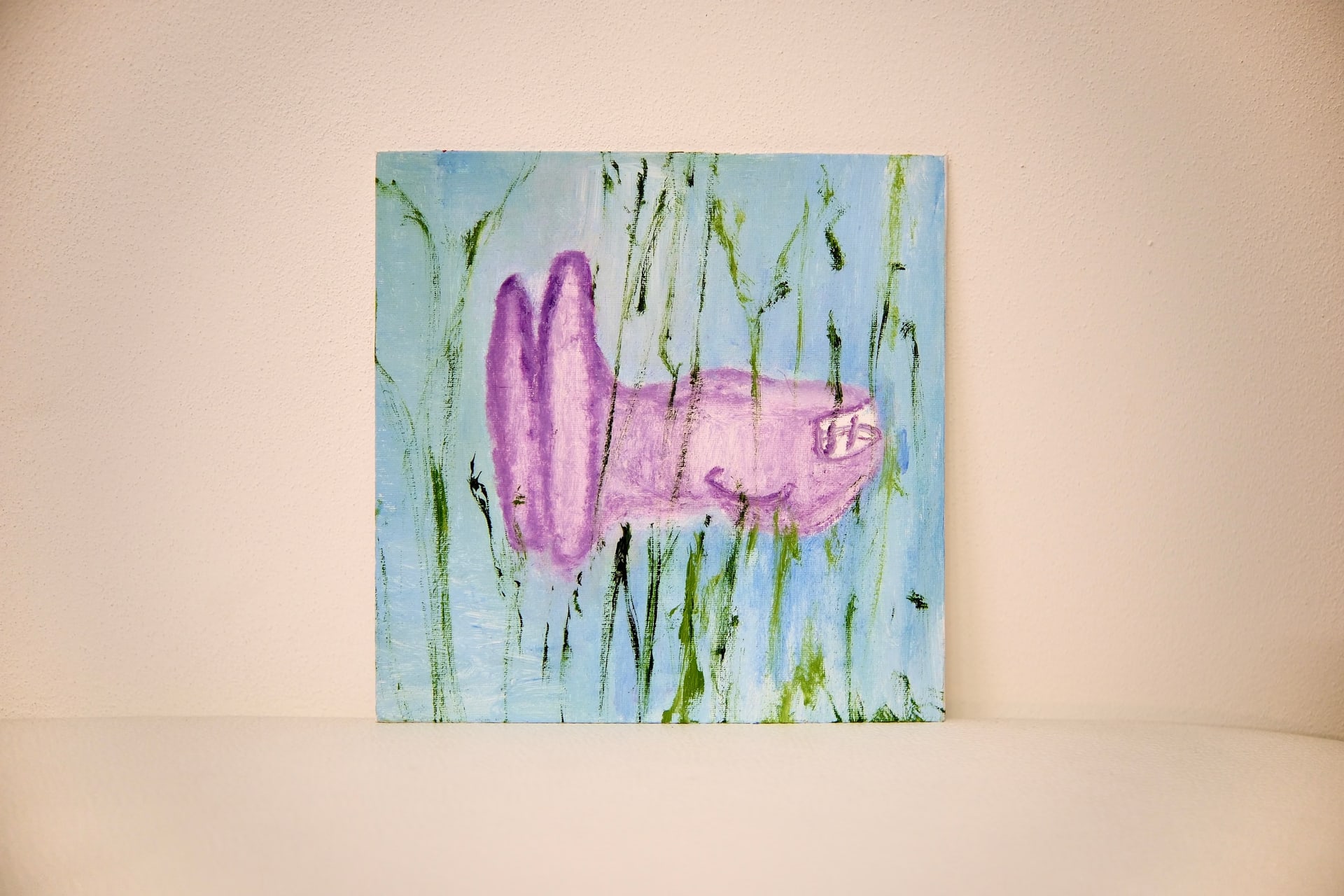 The square canvas propped against a pale wall, its lilac vehicle shape floating among green strokes on pale blue.