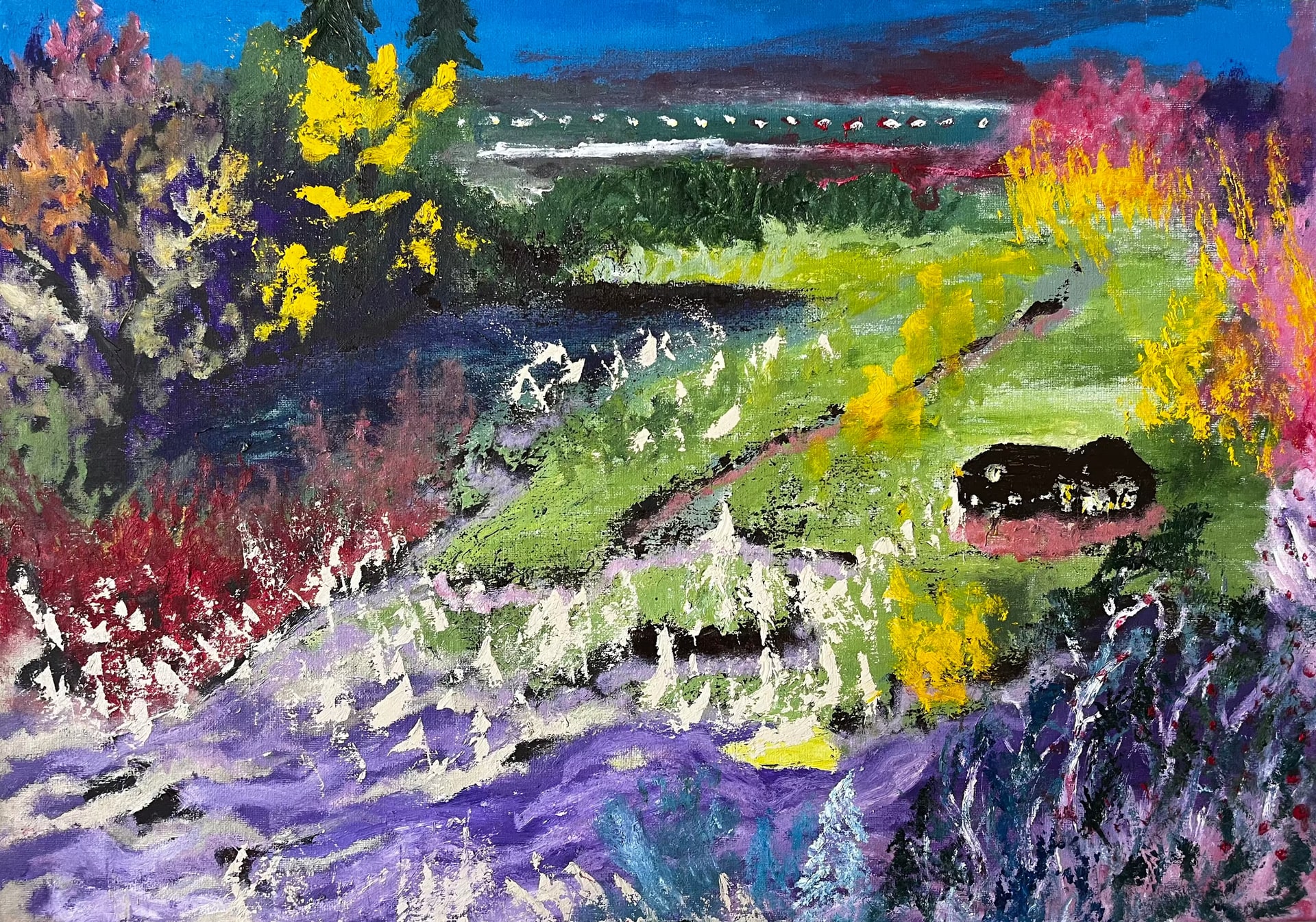 A valley in bloom: a bright green meadow crossed by dark paths falls away from a treeline, banked on both sides by scrub flowering in yellow, orange, crimson and magenta, with a broad lavender slope flecked with cream across the foreground. A small black hut sits on the right-hand slope, and a band of teal water runs under the blue sky behind.